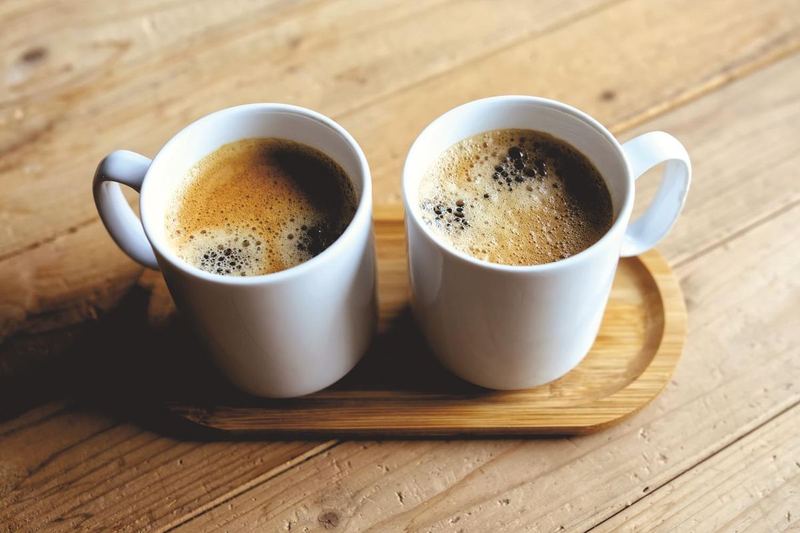 Zwei weiße Tassen mit Kaffee stehen auf einem Holztablett.